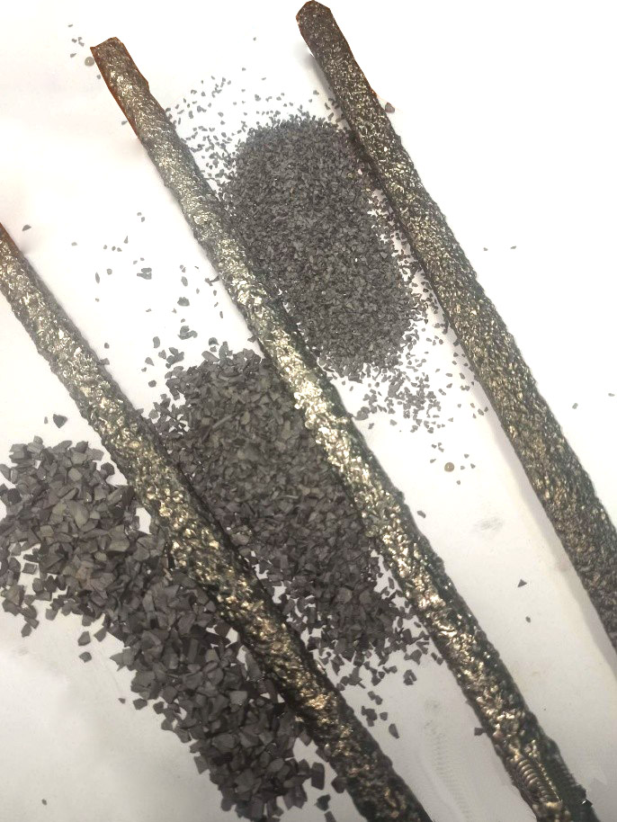 Close-up view of a welded surface showing tungsten carbide particles embedded in a nickel-copper matrix, demonstrating the TechCarbide hard-facing layer applied to drilling tool equipment. The textured, granular surface displays the characteristic appearance of overlay welding with visible carbide distribution across the metal substrate.
