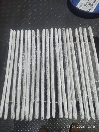 Multiple TechCarbide welding rods arranged in parallel rows on a dark textured metal surface. The rods display a silvery-gray composite appearance with visible tungsten carbide particle distribution embedded in a metallic matrix. A blue container is partially visible in the top left corner. The photograph includes a date stamp showing 28.01.2026 13:10 in the bottom right. The image demonstrates the characteristic hard-facing overlay quality and physical appearance of the welding rods used for drilling tool repair applications.